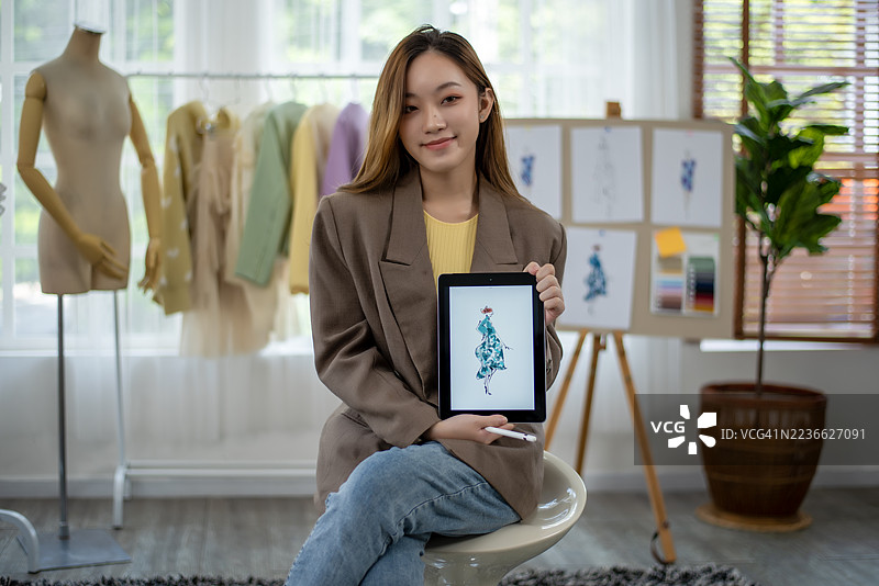 一位美丽的时尚设计师站在她的工作室，手持草图，正在进行新的创作。图片素材