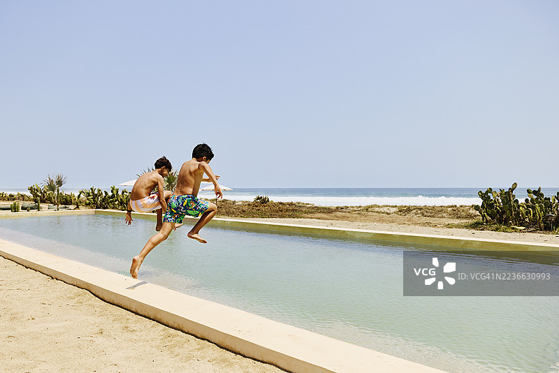 兄弟们跳入海滨度假村游泳池的广角镜头图片素材