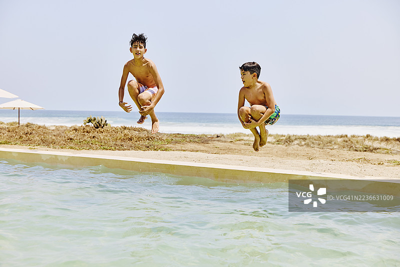 兄弟们在度假村游泳池边缘跳水的广角镜头图片素材