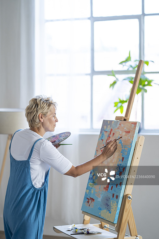 女性艺术家在艺术工作室用画笔和调色板在画布上作画图片素材