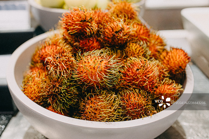 一个大白碗里装满了五颜六色的红毛丹水果。图片素材