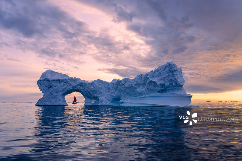 夏季午夜阳光下，冰山拱门与红色帆船组成的壮丽风景图片素材