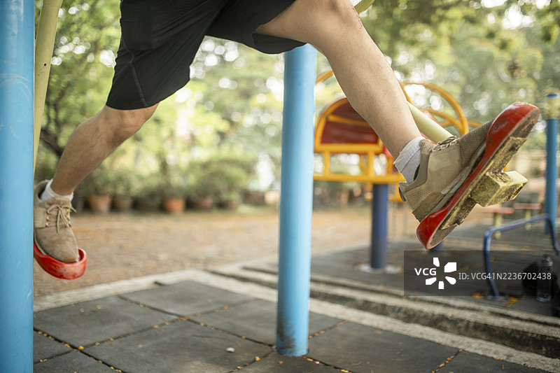 在户外游乐场中，一个人悬空而起，穿着棕色鞋子和红色小丑鞋，场景充满趣味，周围有绿色和黄色的游乐设施。图片素材