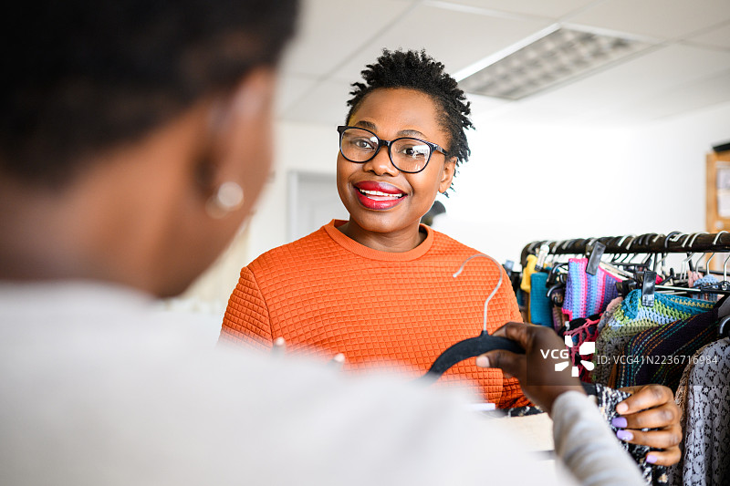 顾客在时装店的衣架上挑选商品，与友好的店主聊天图片素材