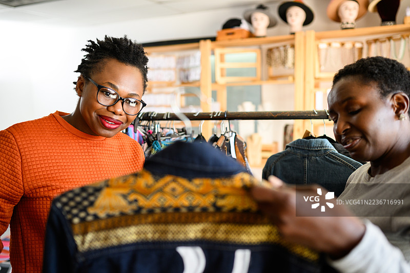 时装精品店里，一位女店主和顾客在购物体验中欣赏一件精美的手工夹克。图片素材