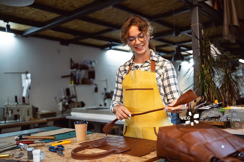 工匠在工作坊中穿着黄色围裙和眼镜制作皮革手提包图片素材