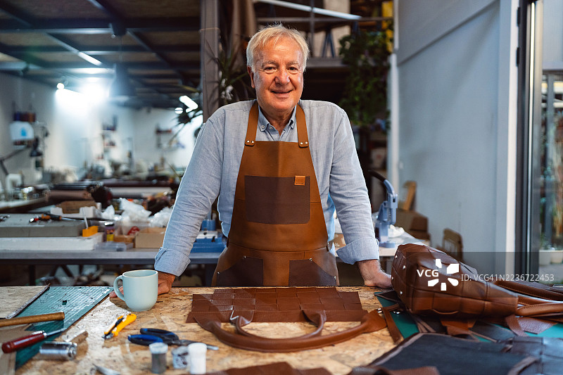 老年皮革工匠在工作室中，周围是手工制作的物品和工具的肖像图片素材