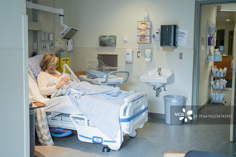 现代产房中，母亲与新生儿在医院床上，周围有医疗设备。图片素材