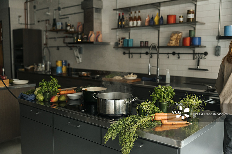 厨房岛上的玻璃陶瓷炉上放着炖锅，里面有蔬菜。图片素材
