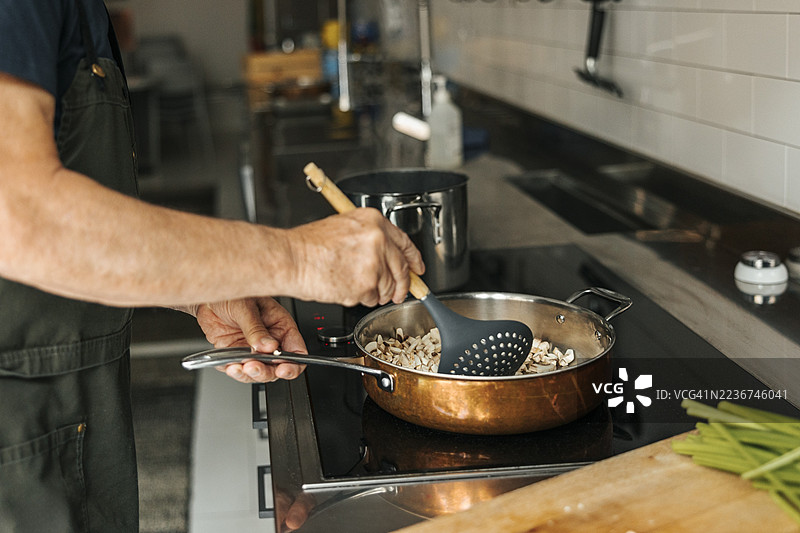 老年男子在商业厨房的烹饪课堂上，用玻璃陶瓷炉炒蘑菇。图片素材