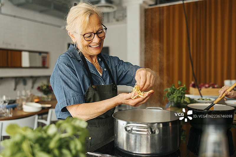 微笑的年长女性非传统学生在商业厨房的课堂上检查正在煮的意大利面图片素材