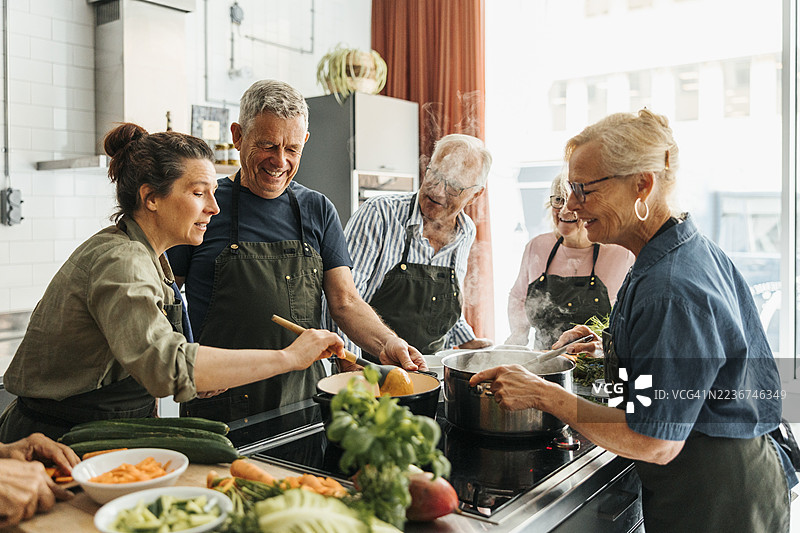 女厨师在商业厨房的烹饪课堂上检查由资深男士制作的酱汁的稠度图片素材