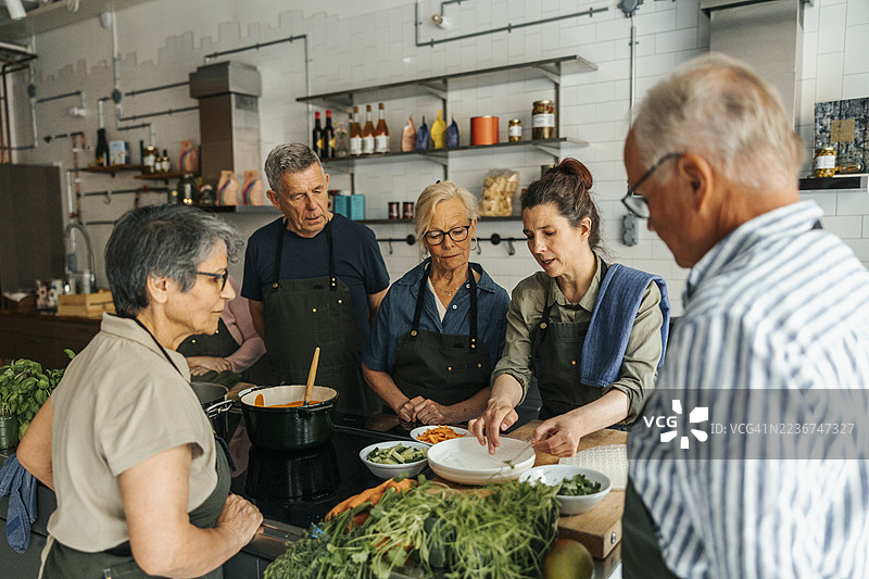 女厨师在商业厨房的烹饪课堂上，向高级学生讲解如何将米纸浸入水中。图片素材