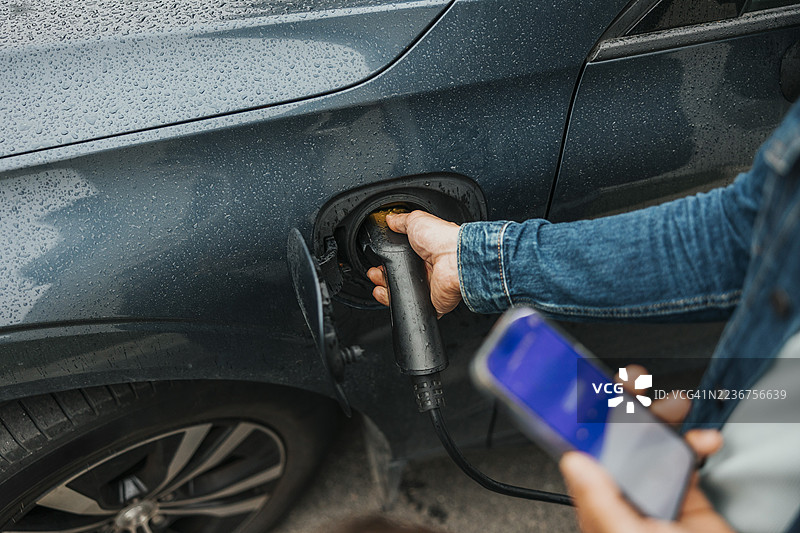 高角度视图的男子在充电电动车，同时手持智能手机图片素材