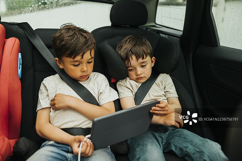 兄弟们坐在车后座上观看平板电脑图片素材