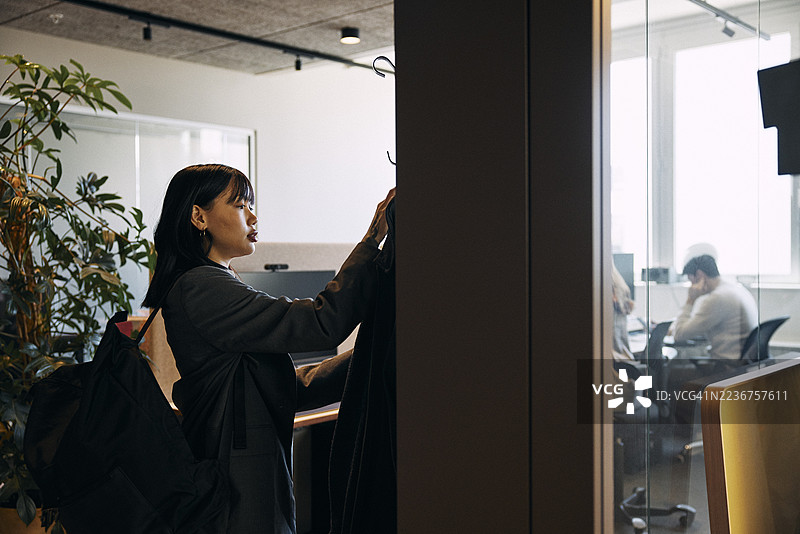 女企业家在进入办公室时将外套挂在衣架上图片素材