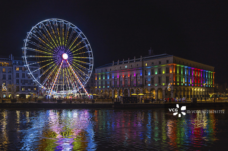 五彩斑斓的摩天轮和市政厅在法国巴约讷的河流中倒影，圣诞夜的景象。图片素材