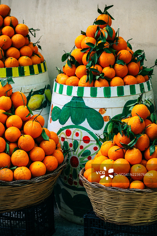 西西里市场中编织篮子和彩绘陶瓷桶里的鲜艳橙子堆。图片素材