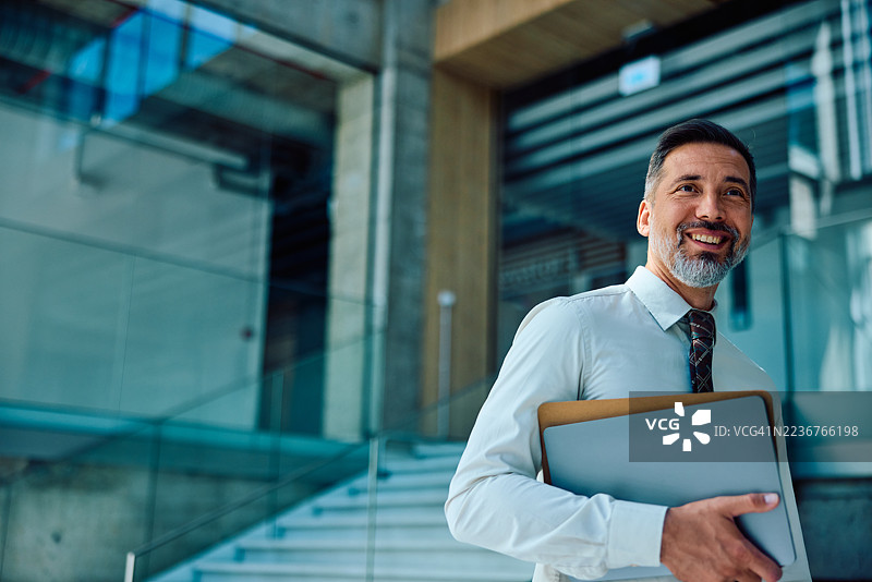 自信的中年男商人在户外走动，手里拿着笔记本电脑图片素材