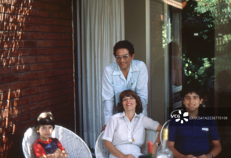 1981年，智利圣地亚哥，一位母亲、一位父亲和他们的两个年幼儿子坐在柳条椅上的老照片图片素材