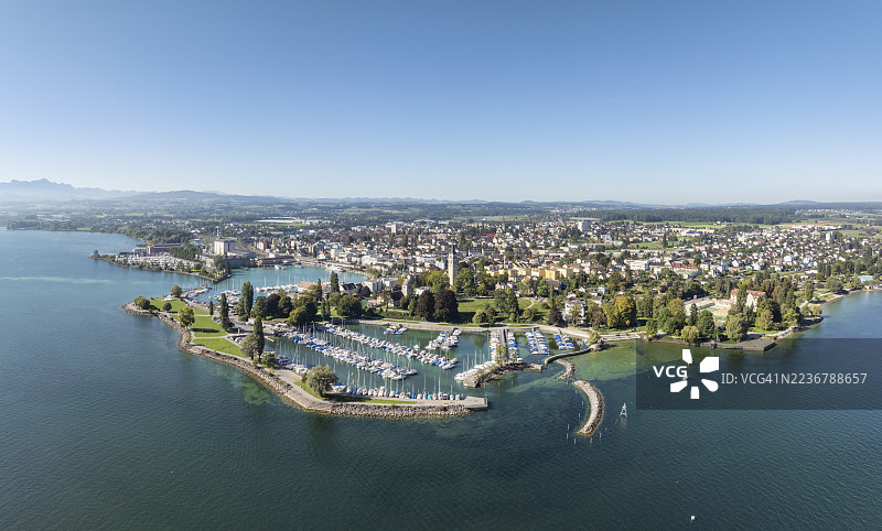 从空中俯瞰康斯坦茨湖畔的罗曼斯霍恩镇，包括港口区、渡轮码头、游艇码头和海滨公园。画面最左侧可见桑蒂斯山。这是瑞士图尔高州的一幅全景图。图片素材
