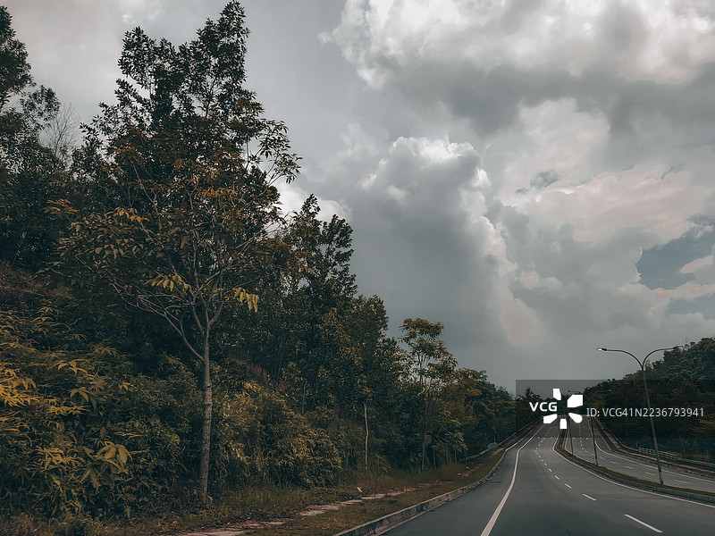 空荡荡的公路蜿蜒穿过郁郁葱葱的山丘，天空云层变幻，暗示着旅行与自由，马来西亚科塔马斯公园。图片素材