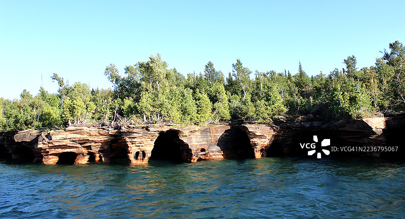 美国使徒群岛沿着森林海岸线的自然岩石形成和海洋洞穴的美丽景观，蓝天清澈。图片素材