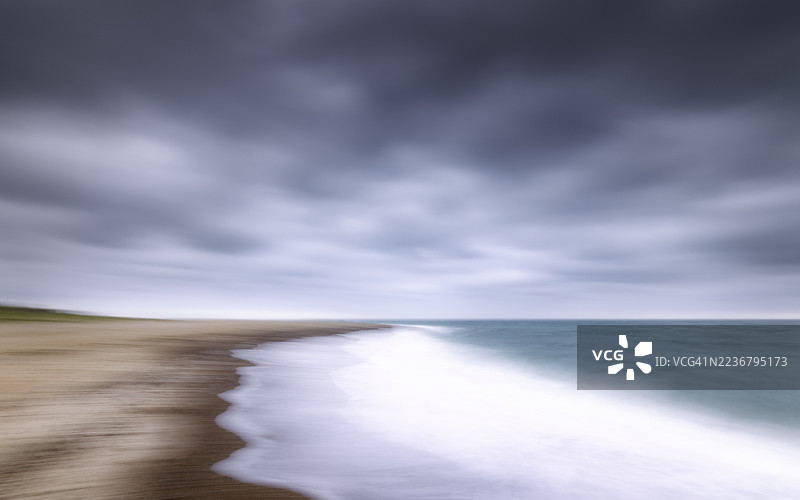长时间曝光的宁静海滩，模糊的海浪和戏剧性的多云天空图片素材