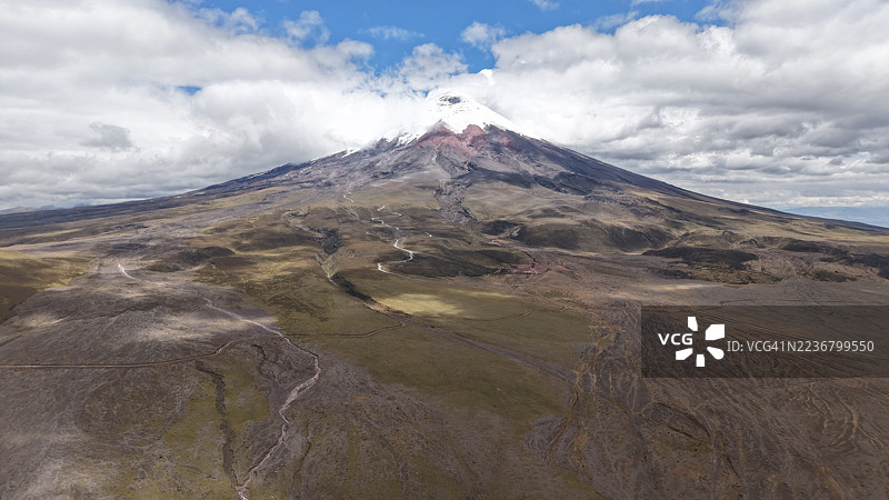雄伟的火山景观，雪顶在多云的天空下，展现出崎岖的地形和蜿蜒的小径图片素材