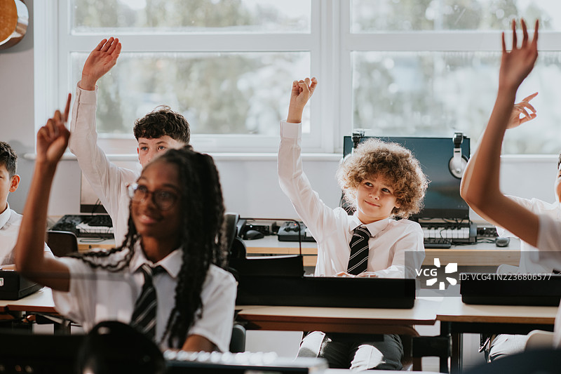 一个青春期前的孩子在课堂上专注地举手参与讨论。图片素材