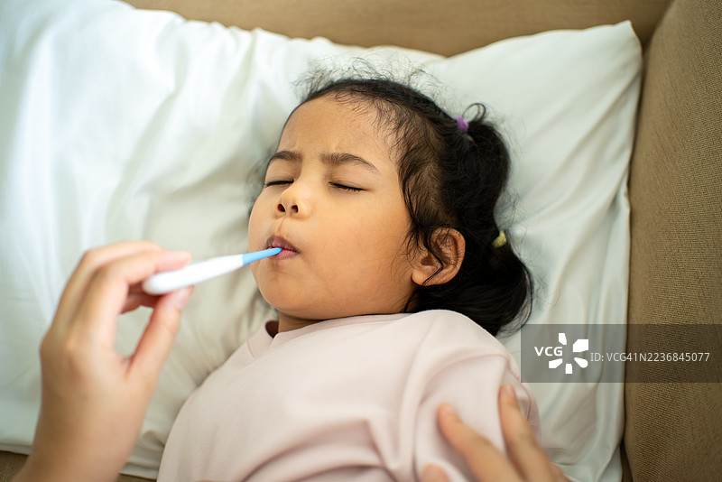 母亲在家中用数字温度计测量生病孩子的体温，关心孩子的健康保险和家庭医疗保障。图片素材