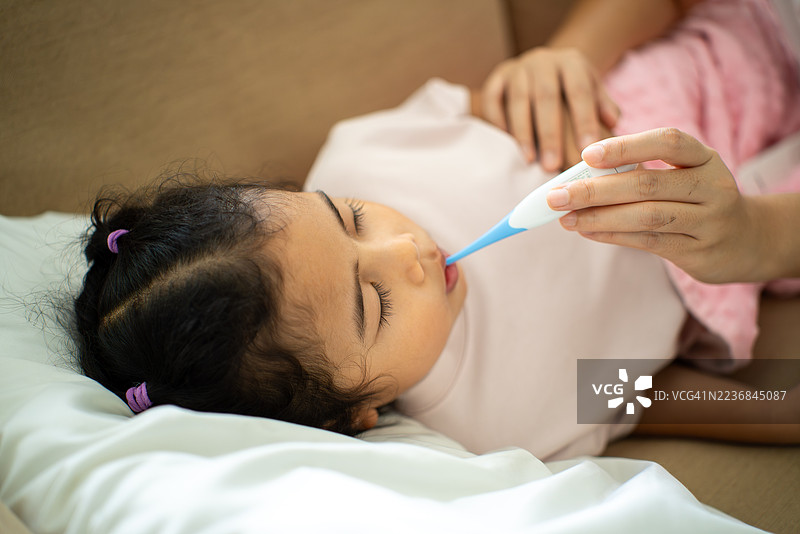 母亲在家中用数字温度计测量生病孩子的体温，父母关心孩子的健康保险支持和家庭医疗保障。图片素材