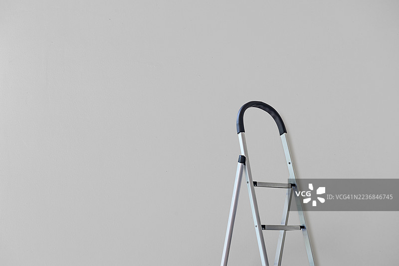 黑色手柄的铝制梯子靠在白色混凝土墙背景上图片素材