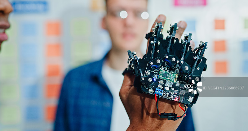 两名男性工程师软件开发人员在办公室检查一个机器人手原型，进行开发和编码任务的集成。人工智能与编程。图片素材