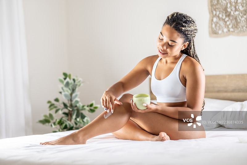 女性在卧室的床上涂抹身体乳，展现优美身姿。护肤、水疗、健康与化妆品理念。图片素材