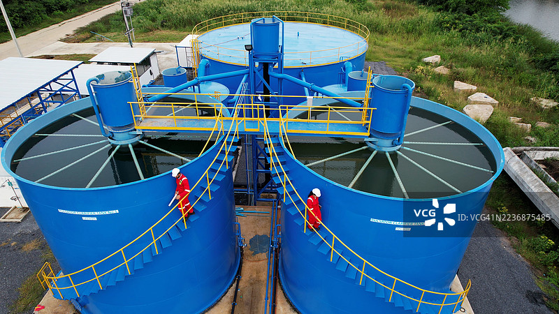 两名穿着红色工作服和个人防护装备的工业工人或工程师正走上楼梯，准备在大型水箱的顶部进行工作，水处理设施，市政水处理厂。图片素材