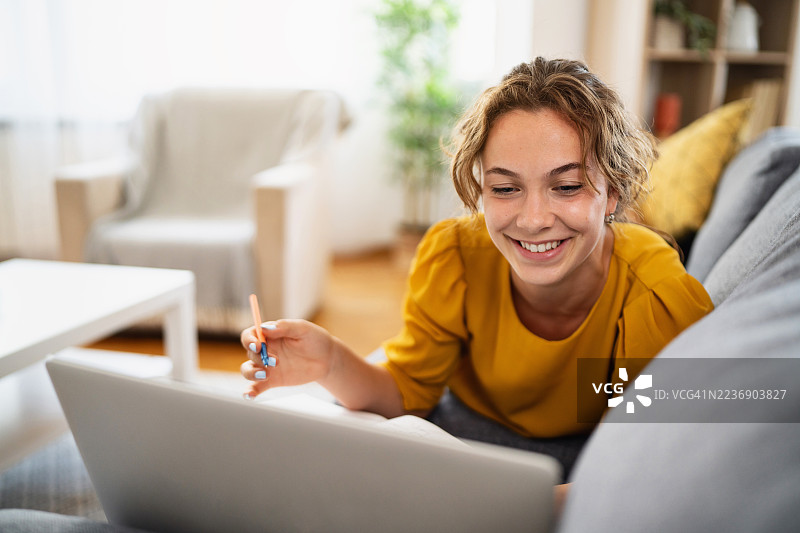 微笑的年轻女性在家躺着使用笔记本电脑图片素材