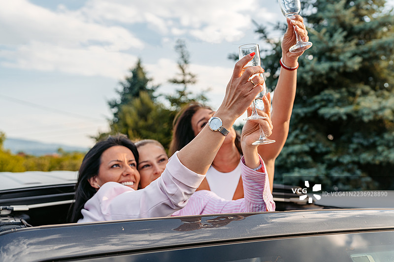 三位中年女性在户外从车顶喝香槟图片素材