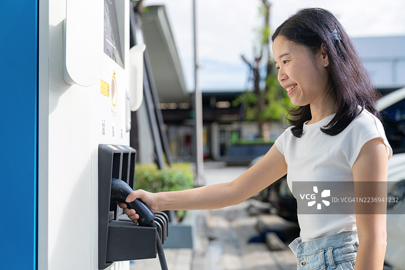 亚洲女性手持电动车充电线，清洁科技概念图片素材