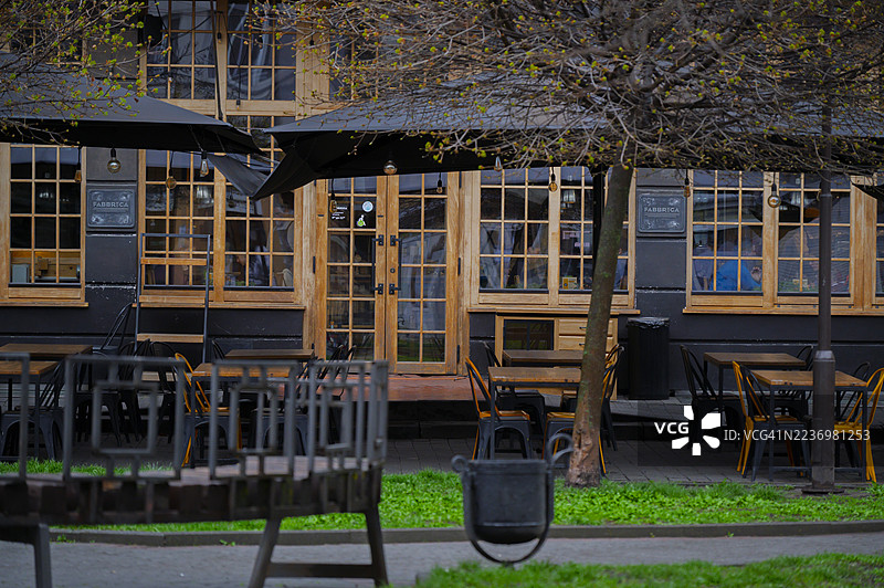 阴天的咖啡馆外观，设有户外座位和城市树木的新春叶子图片素材