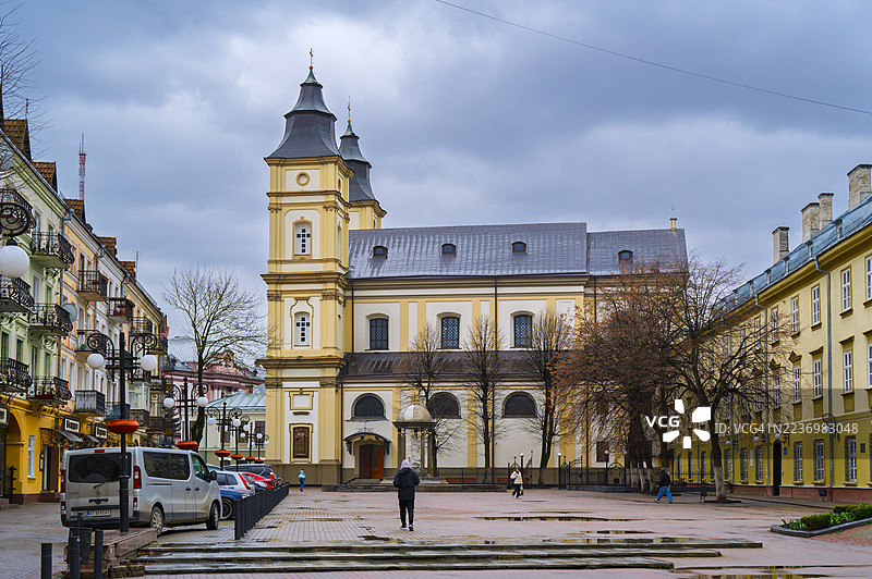 乌克兰伊万诺-弗兰基夫斯克一个潮湿的城市广场上，一座历史建筑赫然矗立，周围环绕着历史悠久的欧洲建筑，天空多云。图片素材