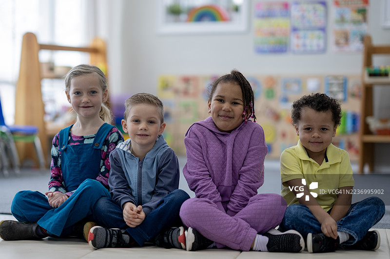四个孩子在明亮的教室里友好地坐在一起，面带微笑。图片素材
