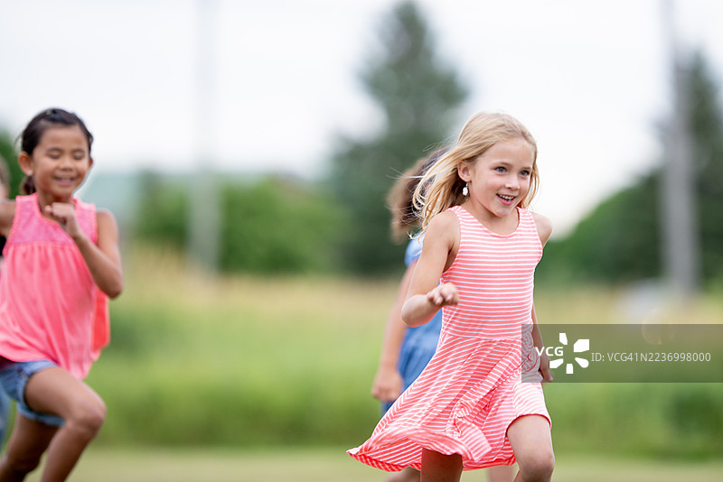 孩子们在户外奔跑：阳光明媚的田野中快乐的女孩们穿着粉色条纹裙子玩耍图片素材