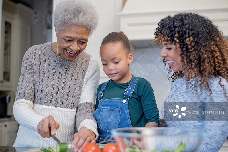 祖母、母亲和孩子在明亮的厨房里一起做饭，家庭亲密时刻图片素材