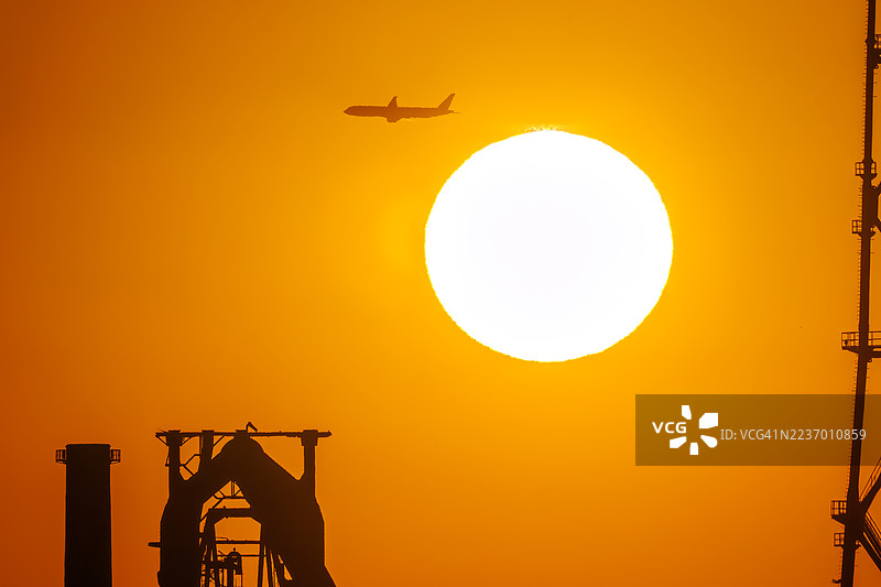 第一缕阳光与一架客机和鸟的剪影。它即将降落在附近的羽田机场。第一缕阳光从运河对岸的烟囱和电厂、钢铁厂上升。横滨，神奈川。图片素材