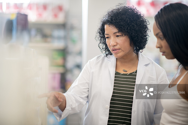 药剂师穿着白大褂在店内向顾客解释药物选择图片素材