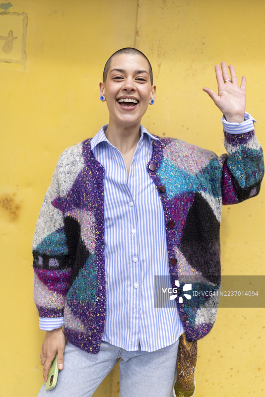 微笑的女性在黄色背景前挥手图片素材