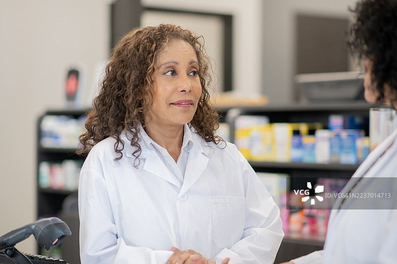 穿着白大褂的药剂师在繁忙的商店药房柜台协助顾客图片素材