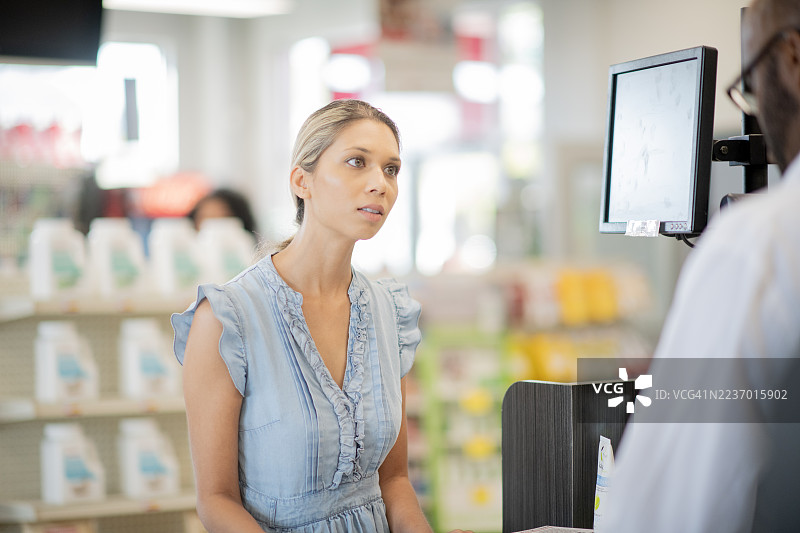 药店柜台前的顾客，背景有显示器和货架图片素材