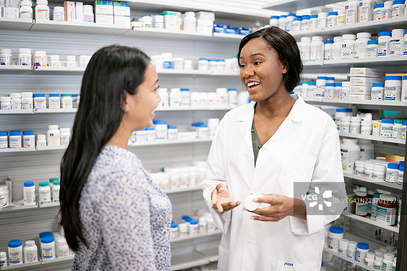 穿白大褂的药剂师在繁忙的药房走道中向顾客解释药物图片素材